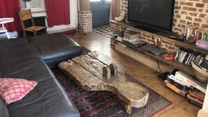 A living room with a brick wall, a black leather sofa, a wooden coffee table, a TV on a brick shelf, and a bookshelf filled with books and games.
