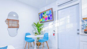 Une pièce moderne avec une porte blanche, une table ronde accompagnée de deux chaises bleues, un tableau abstrait aux couleurs vives et une plante en pot.