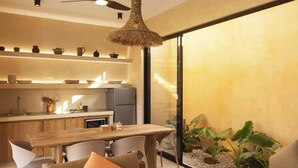 A modern kitchen with wooden cabinets, a dining table, and chairs. There is a large window with a view of plants outside.