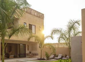 A modern building with a pool area, outdoor seating, and palm trees.