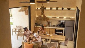 A modern kitchen with wooden cabinets, a dining table, and chairs. There is a hanging light fixture above the table.