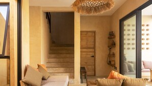 A modern interior with a wooden staircase, a sofa with cushions, a wooden coffee table, and a large window with a view.