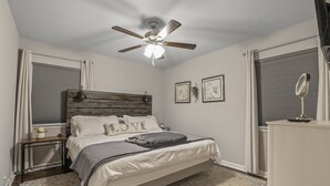 Una camera da letto con un letto, una ventola a soffitto, un comodino, una cassettiera, uno specchio e due quadri appesi al muro.