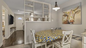 Zona pranzo con tavolo ricoperto da una tovaglia gialla e blu a motivi decorativi, circondato da sedie bianche.