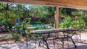 A patio with a table and chairs, surrounded by lush greenery and a swimming pool. - 3-bedroom villa in gorgeous Ngaparou with WiFi, AC, 10 min. away from the beach (Ngaparou)