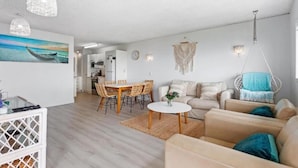 A modern living room with a dining area, a hanging chair, and a kitchen in the background. - Maroochy Sands (Sunshine Coast)