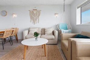 A living room with a white sofa, a beige sofa, a round coffee table, wicker chairs, a macrame wall hanging, and a hanging chair. - Maroochy Sands (Sunshine Coast)