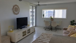A living room with a TV, a dining area with chairs, and a ceiling fan. - Maroochy Sands (Sunshine Coast)