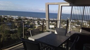Un balcón con mesa y sillas, con vista al mar y casas a lo largo de la costa.