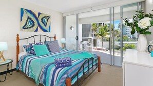 A modern bedroom with a large bed, a balcony with a view, and a white dresser. - Maroochy Sands (Sunshine Coast)