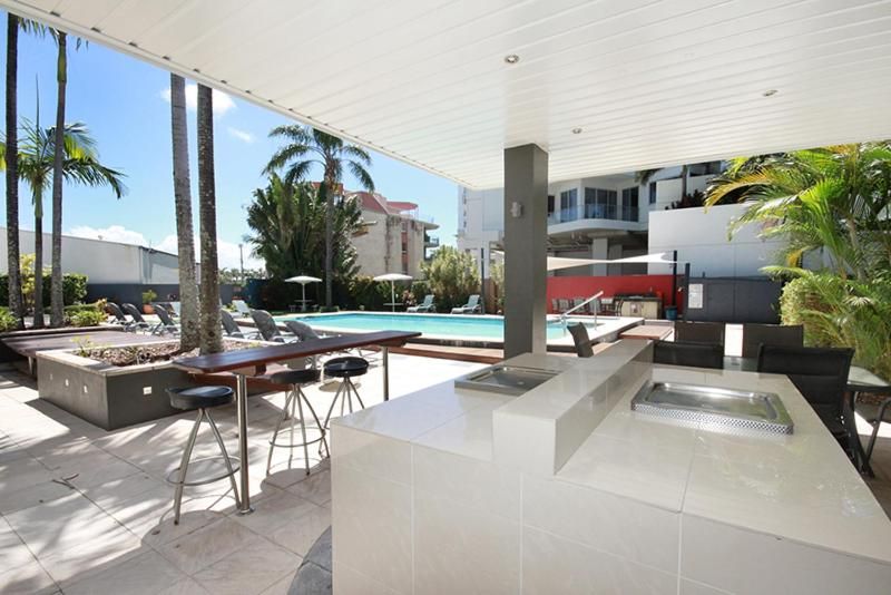 Un área de piscina al aire libre con sillones de descanso, un bar y vistas a un edificio en el fondo.