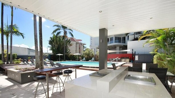 An outdoor pool area with lounge chairs, a bar, and a view of a building in the background. - Maroochy Sands (Sunshine Coast)