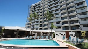 A multi-story hotel with a swimming pool, palm trees, and lounge chairs. - Maroochy Sands (Sunshine Coast)