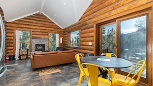 Ein Holzblockhaus-Interieur mit Kamin, Sofa, Esstisch und gelben Stühlen.