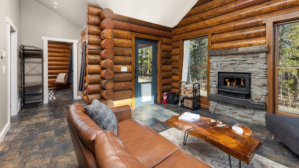Ein rustikales Blockhaus-Interieur mit Kamin aus Naturstein, einer Ledersofa und einem Esstisch.