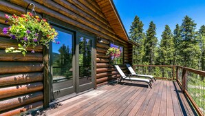 Eine Blockhütte mit einer Holzterrasse, zwei Liegestühlen und hängenden Blumenkörben.