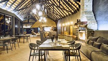 A spacious dining area with high ceilings and exposed beams, a stone fireplace, and modern furnishings.