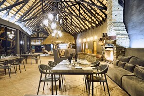 A spacious dining area with high ceilings and exposed beams, a stone fireplace, and modern furnishings. - Ai Aiba The Rockpainting Lodge (Omaruru)