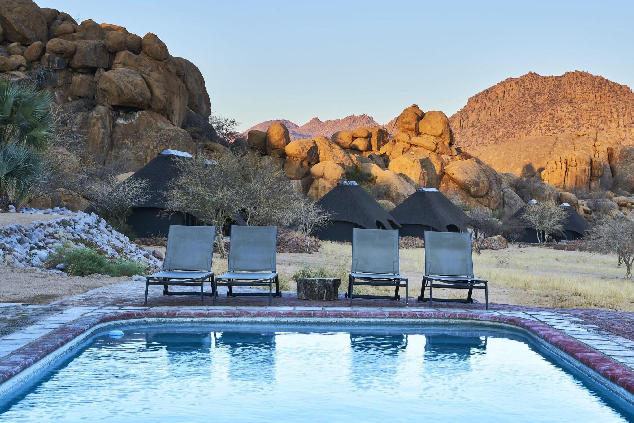 A pool area with lounge chairs and a view of rocky mountains.