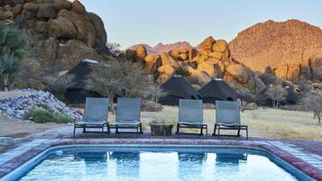 A pool area with lounge chairs and a view of rocky mountains.