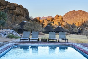 Zona de piscina con sillas de descanso y vistas a montañas rocosas.