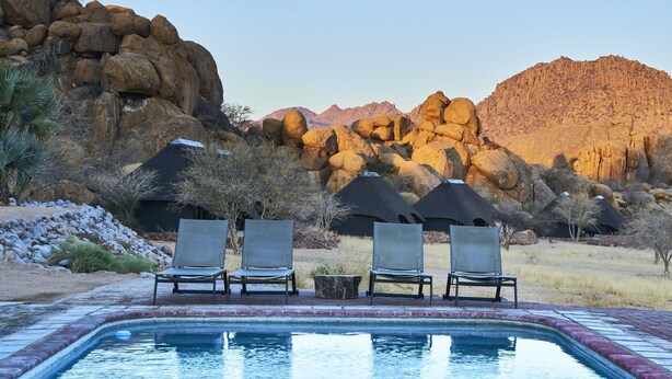 A pool area with lounge chairs and a view of rocky mountains. - Ai Aiba The Rockpainting Lodge (Omaruru)