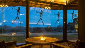 A room with a large window, a round table with candles, and wooden chairs. - Ai Aiba The Rockpainting Lodge (Omaruru)