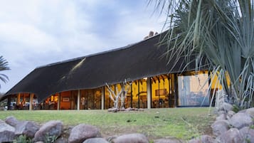 A building with a thatched roof and large windows, surrounded by rocks and grass.