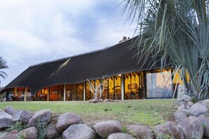 A building with a thatched roof and large windows, surrounded by rocks and grass.
