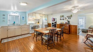 A spacious kitchen with wooden cabinets, a dining table with chairs, a refrigerator, and a ceiling fan.