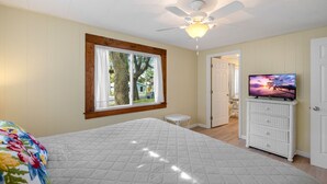 A bedroom with a bed, a ceiling fan, a TV on a dresser, and a window with curtains.