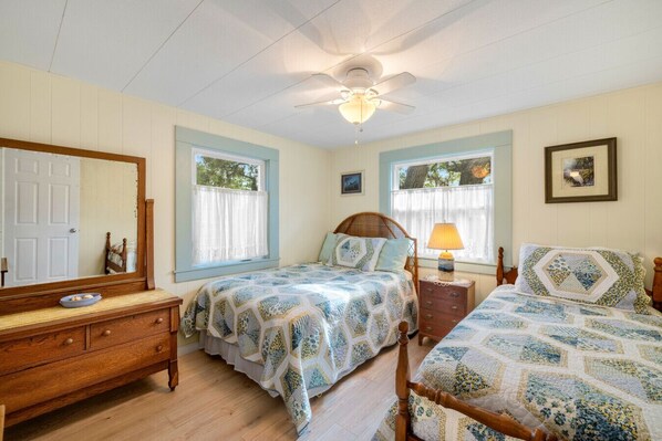 Une chambre avec deux lits, une commode, un miroir et un ventilateur de plafond.