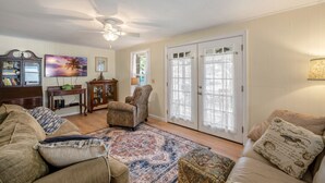 A living room with a sofa, armchair, and a coffee table. There is a television, a cabinet, and a window with curtains.