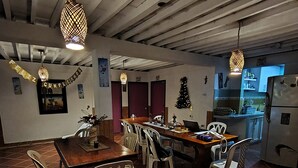 Uma área de refeições com uma mesa e cadeiras de madeira, uma cozinha ao fundo e um pinheiro de Natal.
