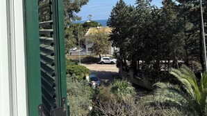 A view through a window with a green frame, overlooking a residential area with trees, a parked car, and a building with a yellow roof. - Villa Rubino Guest house Mondello (Palermo)