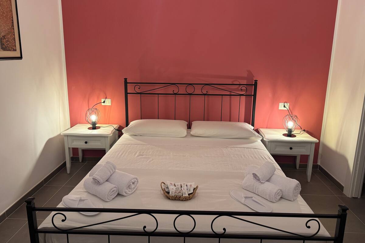 Un lit bien fait, avec du linge de lit et des serviettes blanches, deux tables de chevet avec des lampes et un tableau encadré au mur.