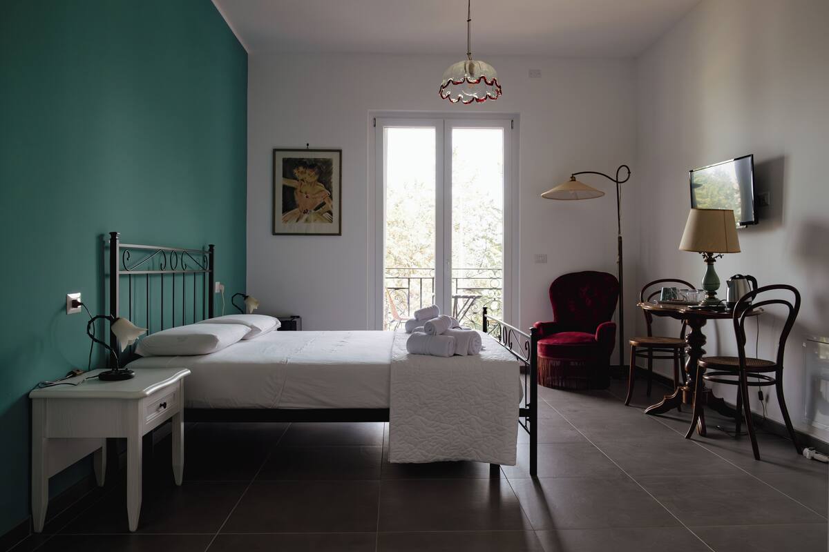 Une chambre à coucher comprenant un lit, une table de chevet, une lampe, une chaise et un téléviseur fixé au mur.