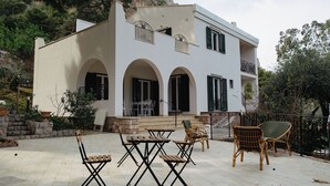 A two-story building with a balcony, outdoor seating area, and a stone wall. - Villa Rubino Guest house Mondello (Palermo)