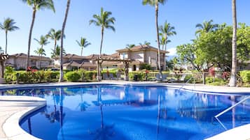 A swimming pool surrounded by palm trees and a building with a tiled roof.