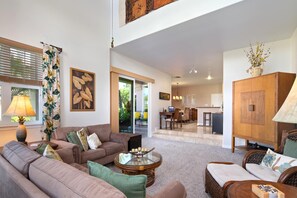 A spacious living room with a sofa, armchairs, and a coffee table. There is a dining area with a table and chairs, and a kitchen in the background.