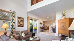 A spacious living room with a sofa, armchairs, and a coffee table. There is a dining area with a table and chairs, and a kitchen in the background.
