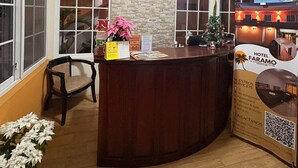 Un espace d’accueil d’hôtel avec un comptoir de réception en bois, une horloge et un appareil de climatisation fixé au mur.