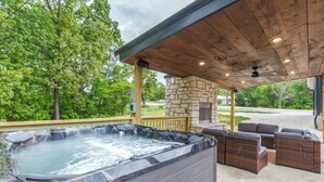 A hot tub under a wooden pergola with stone walls, surrounded by wicker furniture and a stone fireplace. - Spacious 5-bedroom just 1 minute from Bennett Spring State Park! (Lebanon)