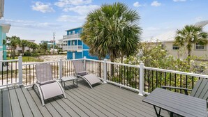 A deck with outdoor furniture, a view of a beach, and palm trees.