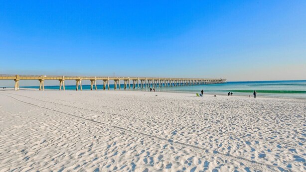 A beach with a pier extending into the ocean, sandy beach, and clear blue sky.