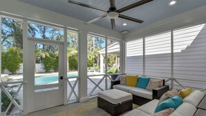 Un área de estar al aire libre techada con ventilador de techo, vista a la piscina y patio con alfombra estampada.