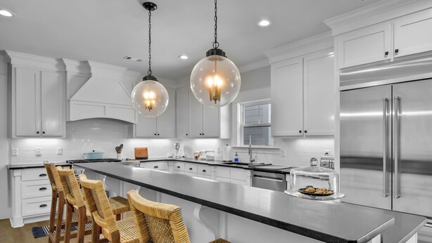 Cocina moderna con armarios blancos, una isla grande con taburetes de bar, electrodomésticos de acero inoxidable e iluminación colgante.