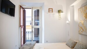 A bedroom with a bed, a TV, a window with shutters, a plant, and a painting. - APARTMENTS THE MUSHROOMS. HISTORICAL CENTER (Sevilla)