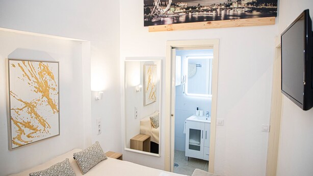 A hotel room with a bed, a large abstract painting, a mirror, a small table with a towel, and a view of a cityscape through a window. - APARTMENTS THE MUSHROOMS. HISTORICAL CENTER (Sevilla)