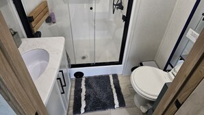 A modern bathroom with a glass-enclosed shower, a white sink, and a toilet. - Spacious 2025 Destination RV Sleeps 9 (Lorena)